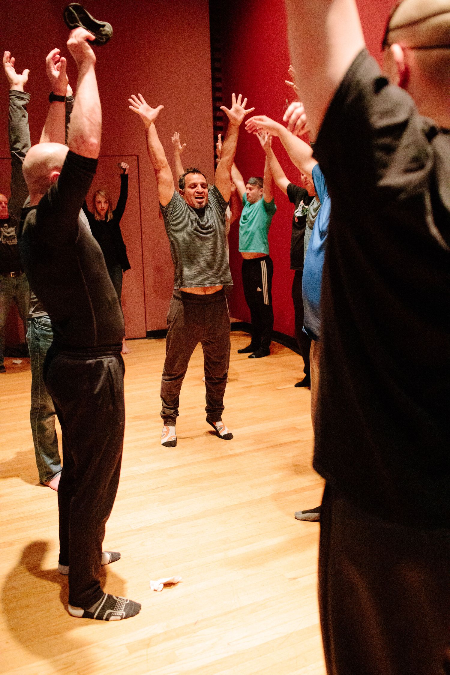 Group of students practicing movement exercises in a dance studio with wooden floors and red walls.