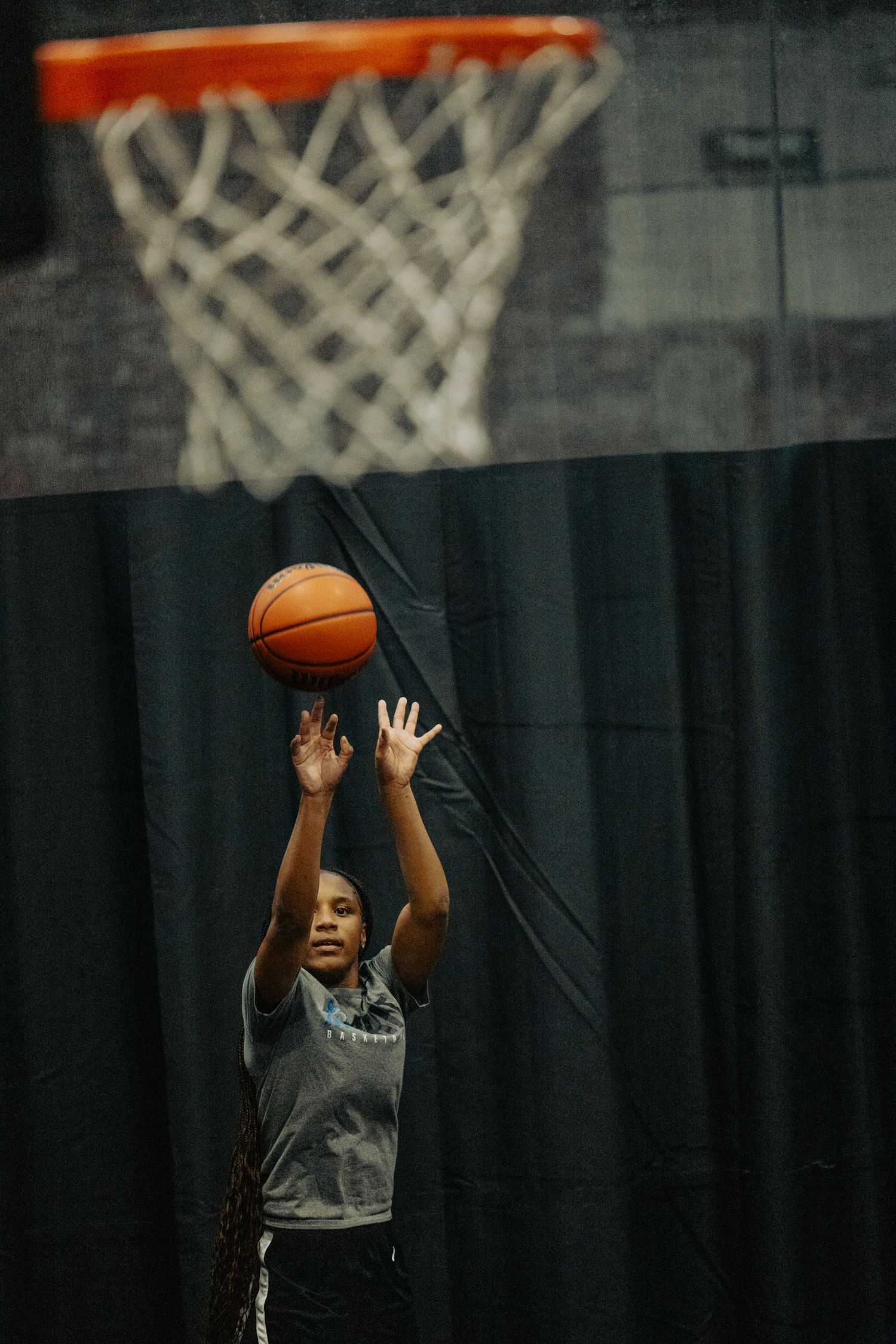 Player practicing basketball shots on indoor court with net visible in background.