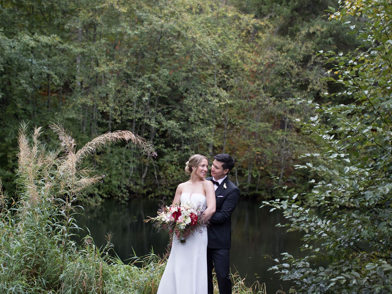 A couple embraces during their outdoor wedding photoshoot surrounded by greenery and trees.