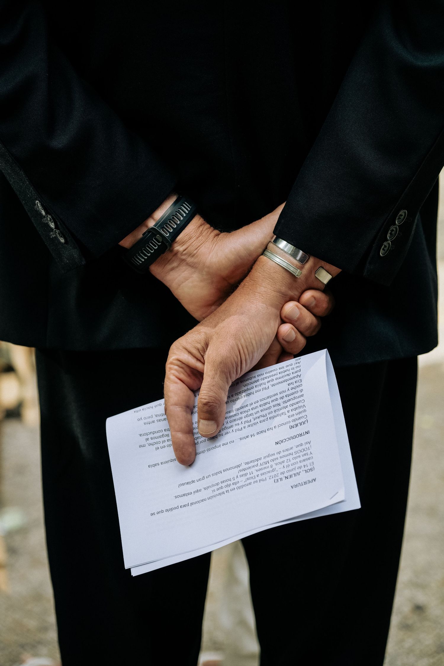 Close-up view of hands with bracelets holding a white document against a dark background.