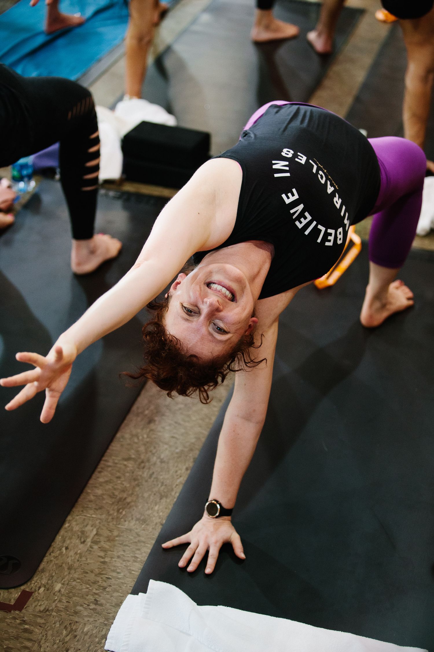Person practicing yoga poses on a black mat during an indoor fitness class.
