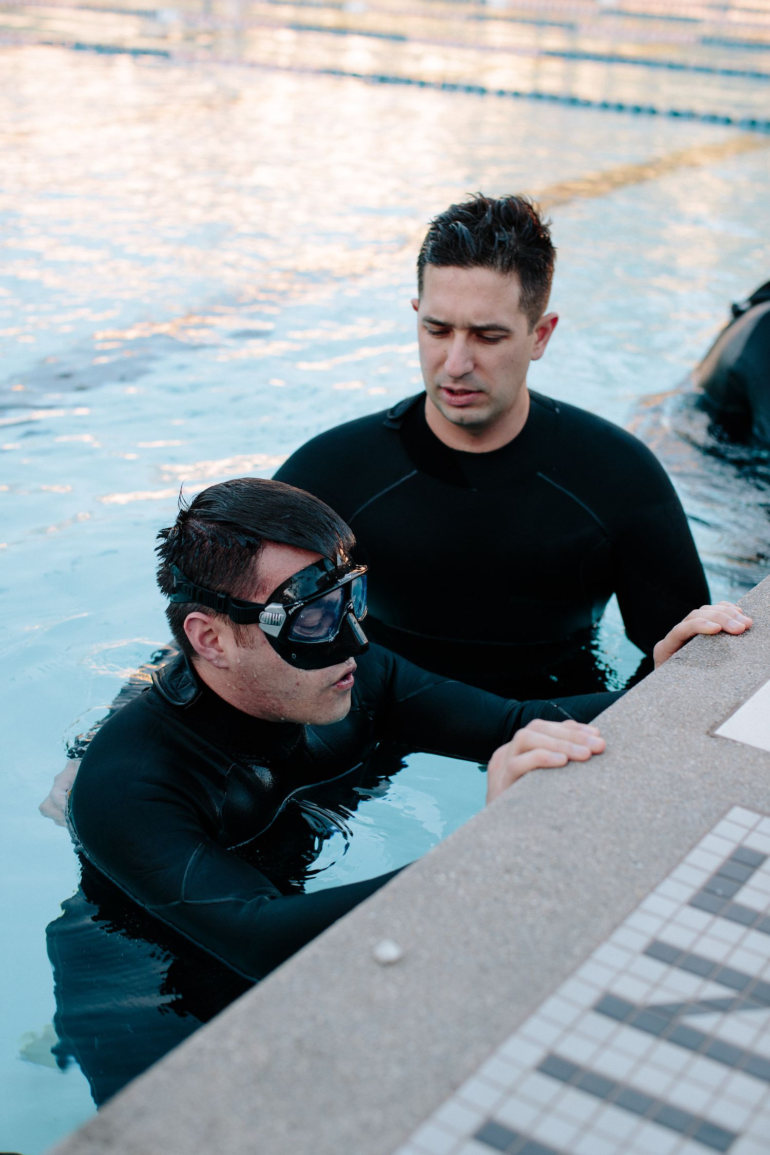 Person in wetsuit and goggles holding onto pool edge during swim training.