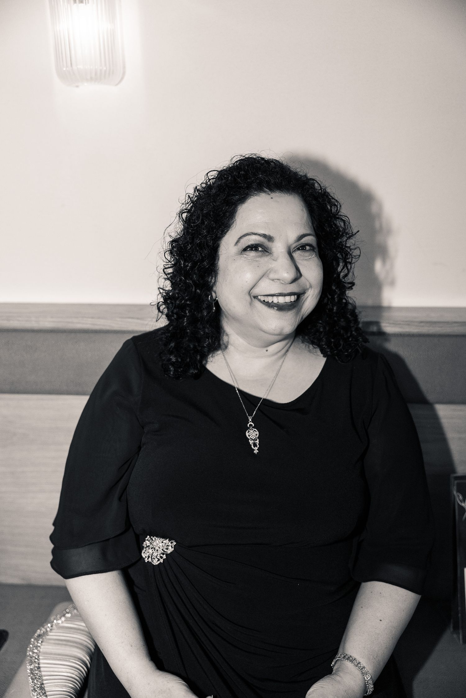 Black and white portrait of someone with curly dark hair wearing a black dress and necklace, smiling warmly.