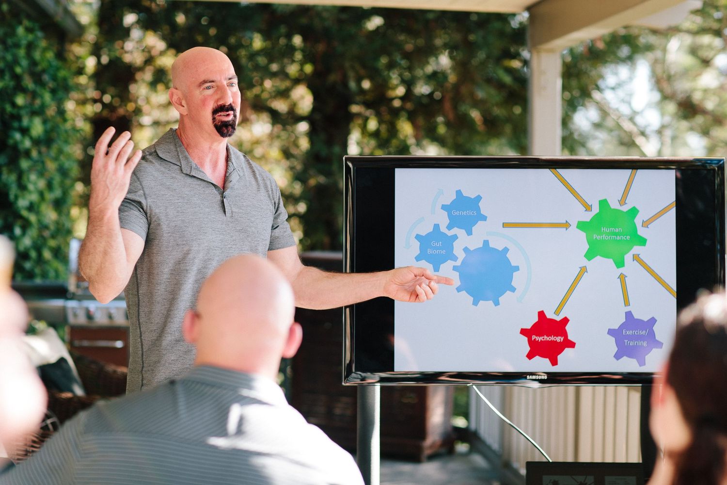 Animated presenter gestures enthusiastically while explaining a colorful diagram during outdoor presentation.