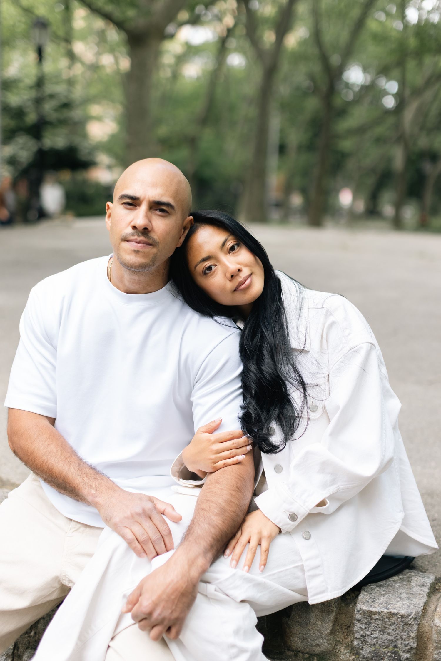 Couple dressed in white sitting together outdoors in a park setting.