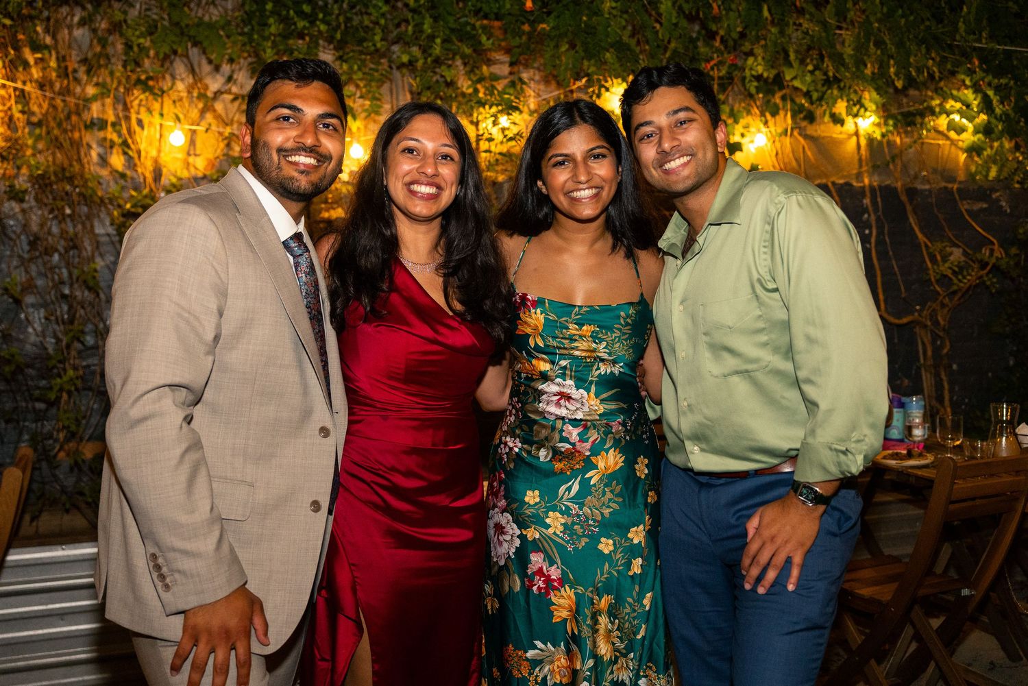 Friends gather for photos under string lights at an outdoor evening celebration.