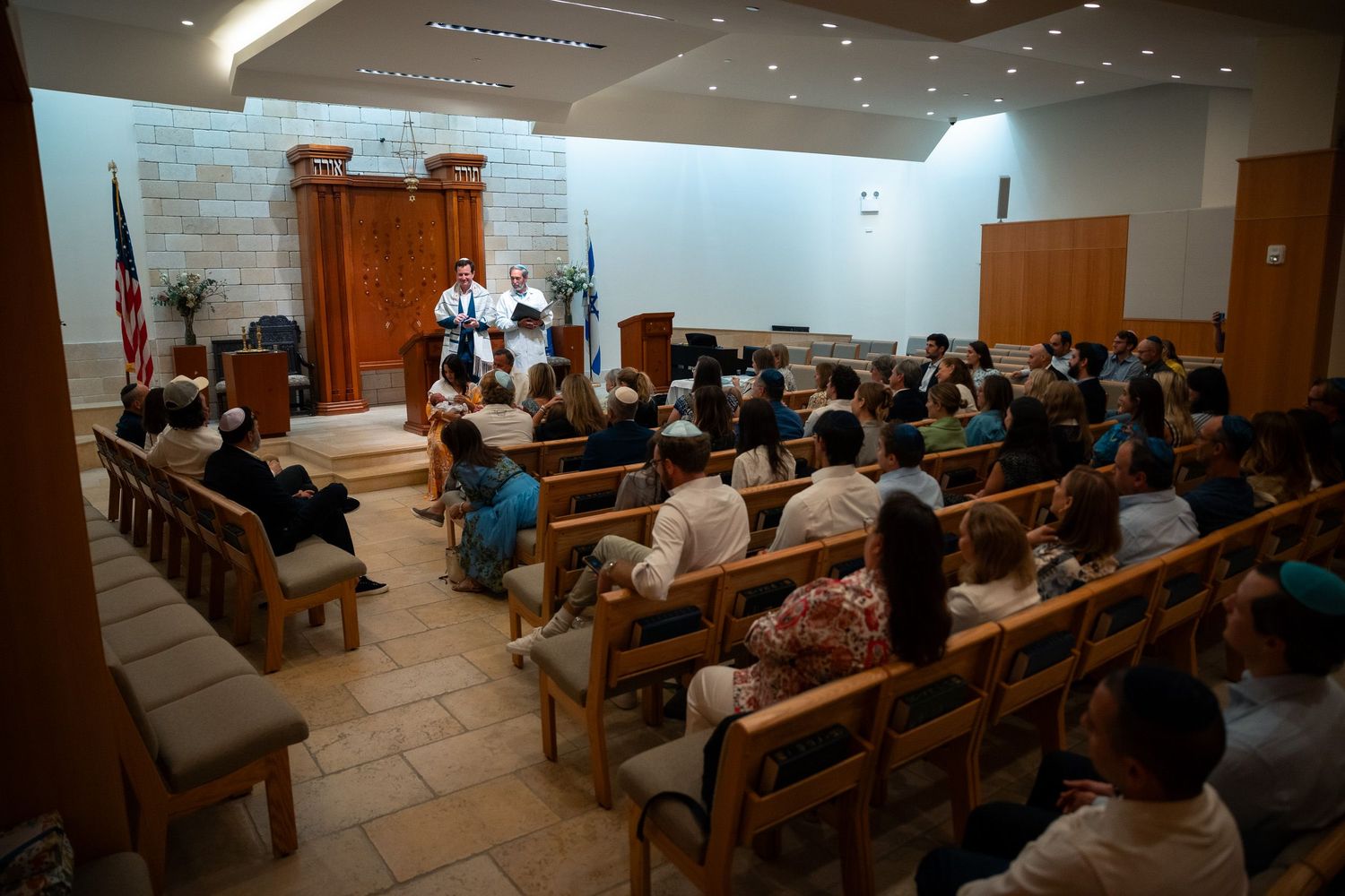 Interior of a modern synagogue or temple during a service with wooden pews.