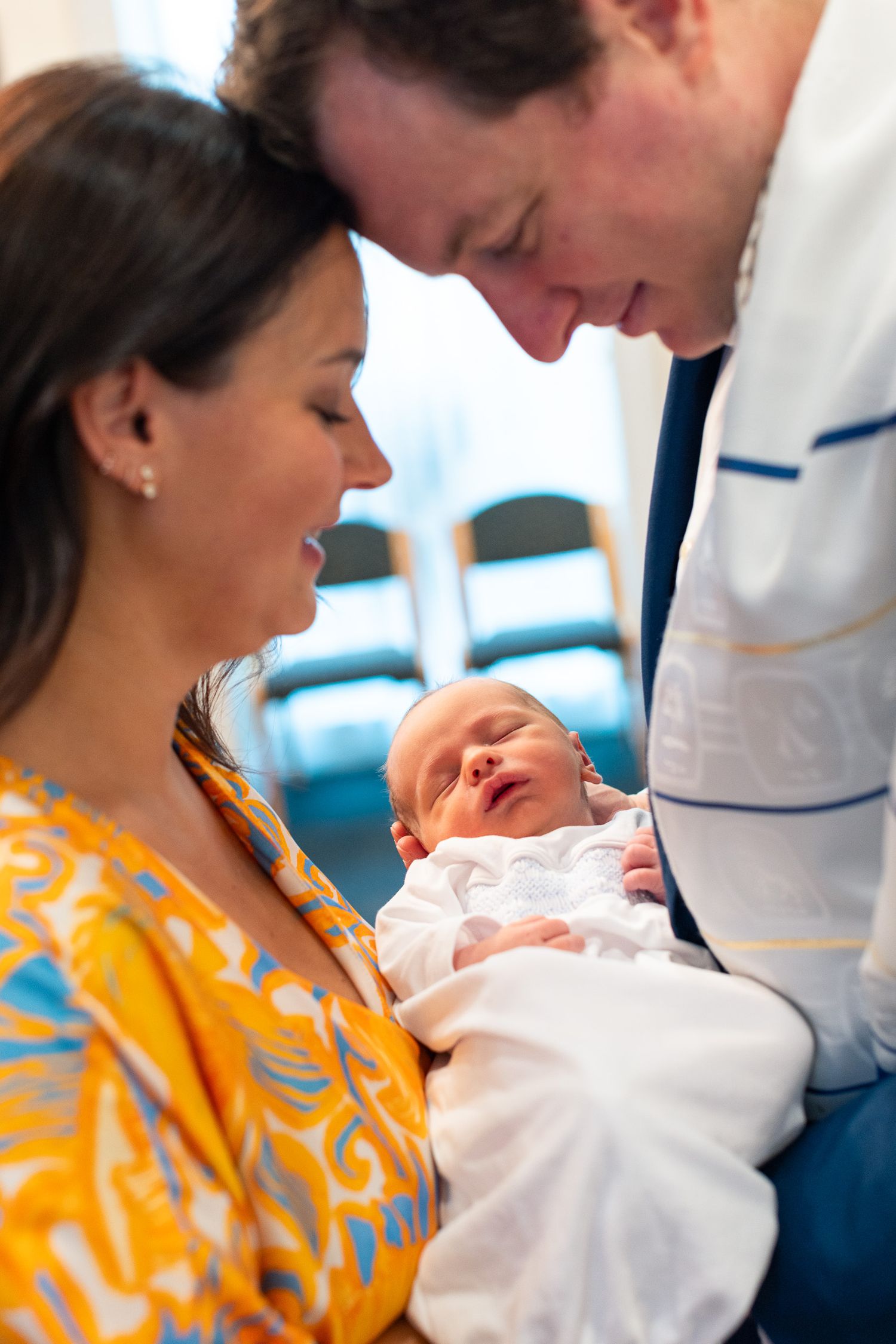 Tender moment as parents admire their newborn baby in white swaddle.