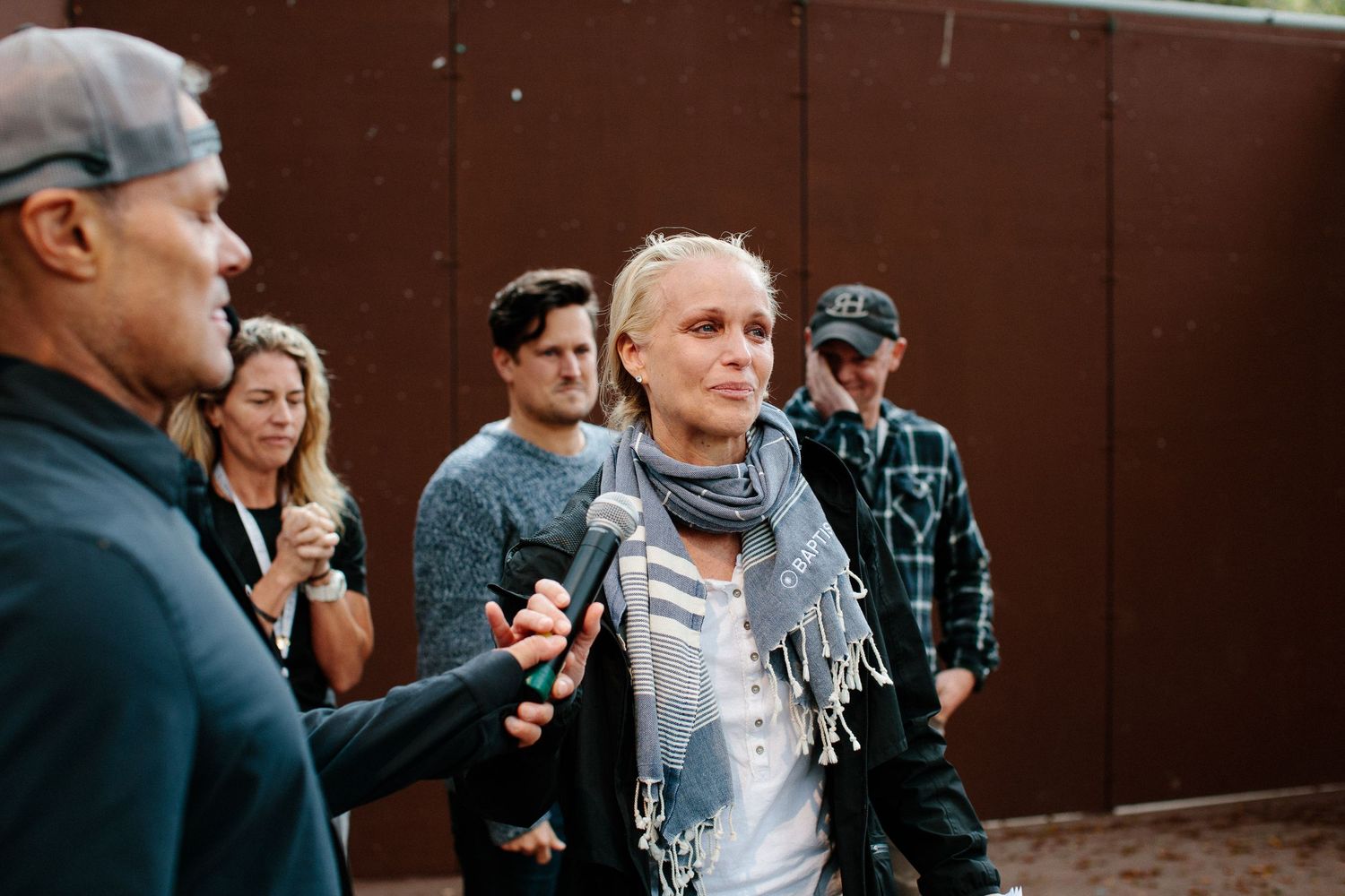 People gathered outdoors against a brown wall backdrop at a casual social event.