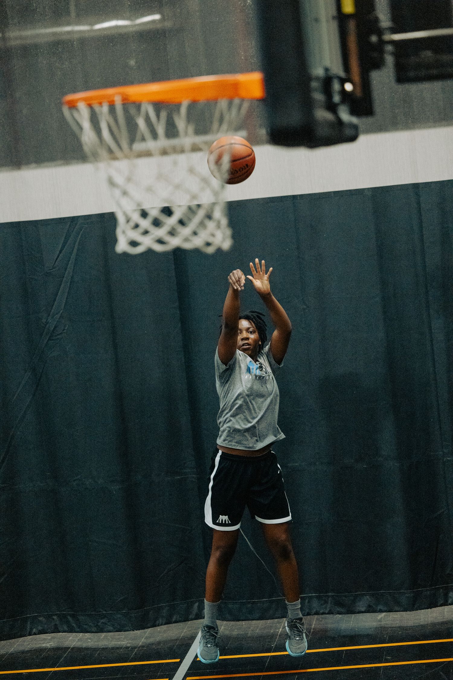 Player jumps while shooting basketball towards hoop during indoor practice.