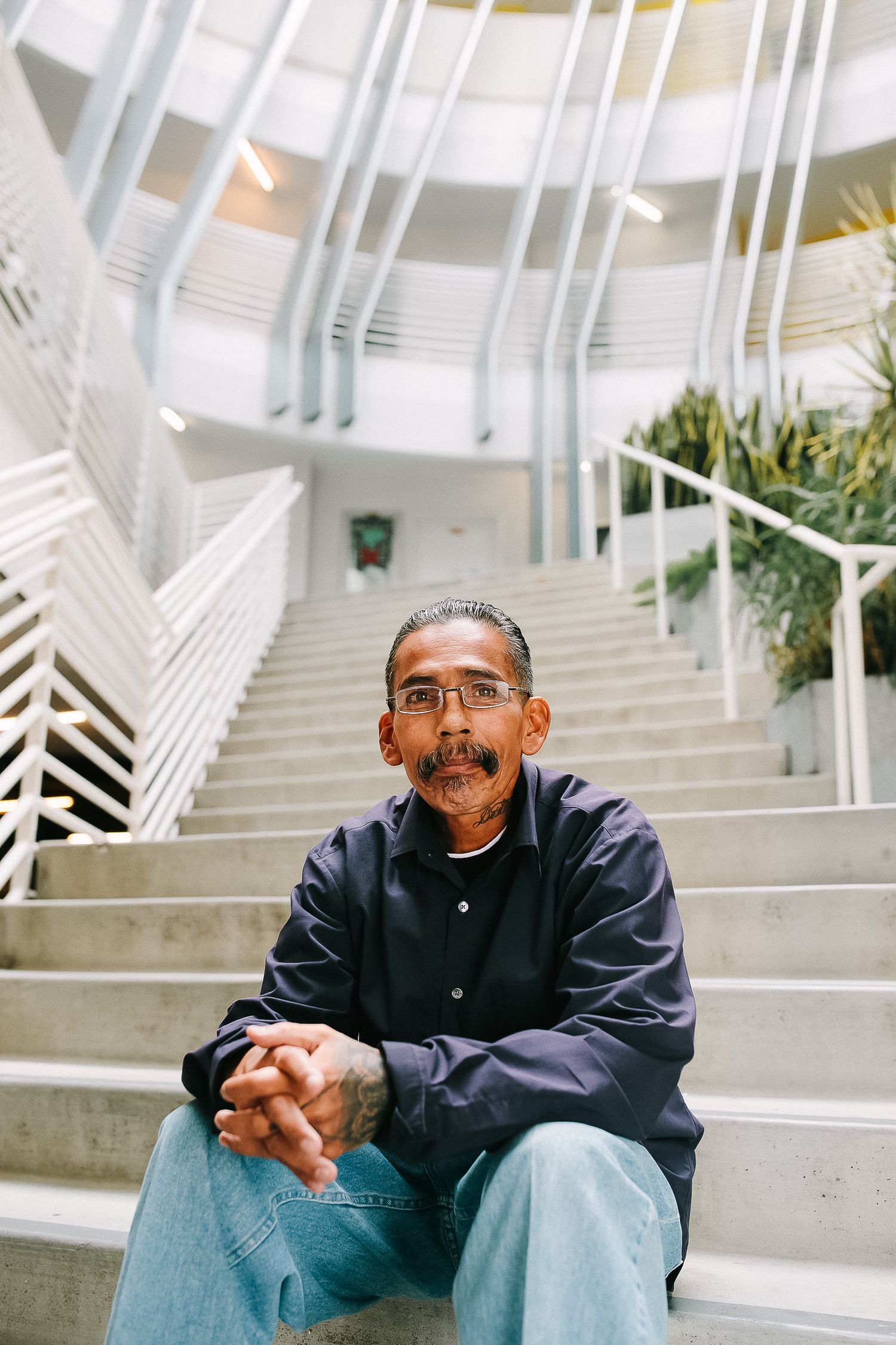 Person in a navy jacket sits contemplatively on concrete steps in a modern architectural space with white beams.