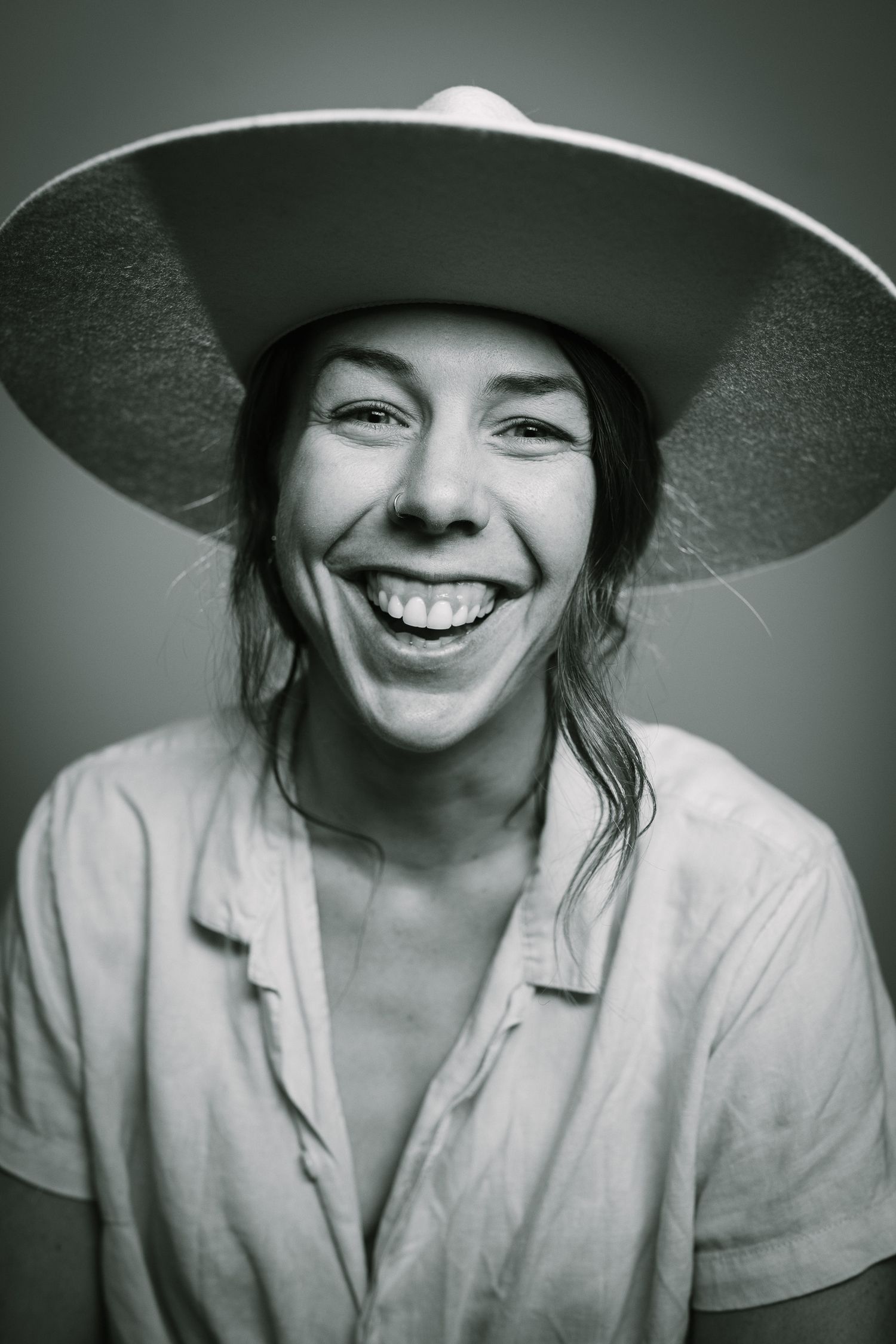 Black and white portrait of joyful person wearing wide-brimmed hat and white button-up shirt.