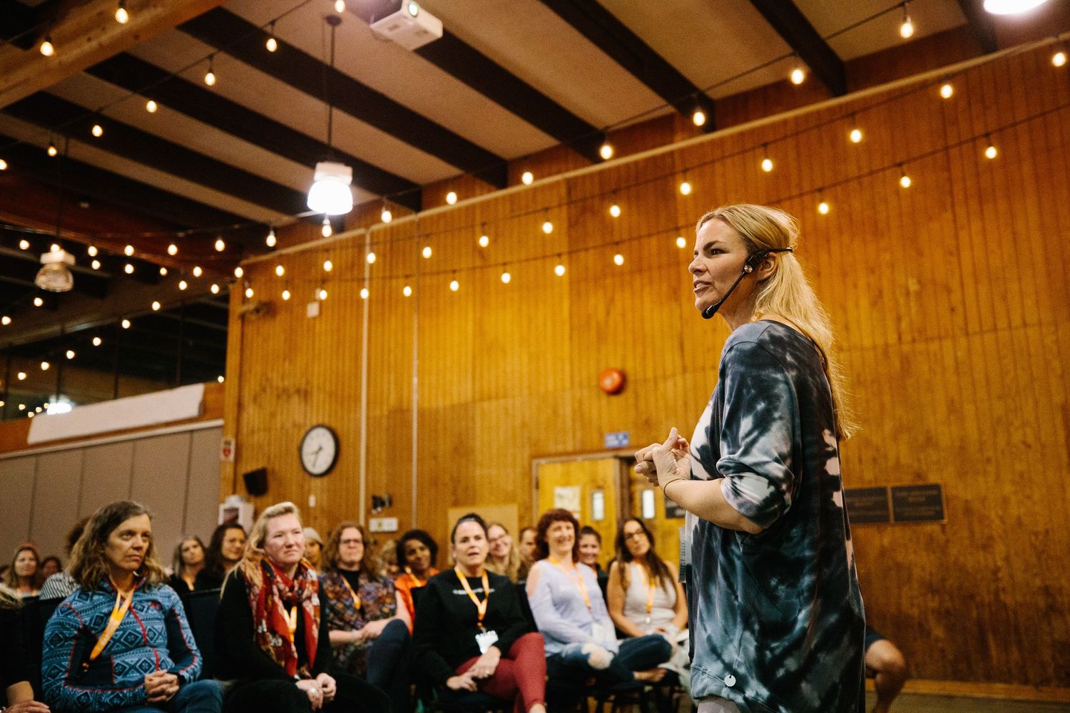 A crowded indoor event space with wooden walls and string lights overhead during a gathering.