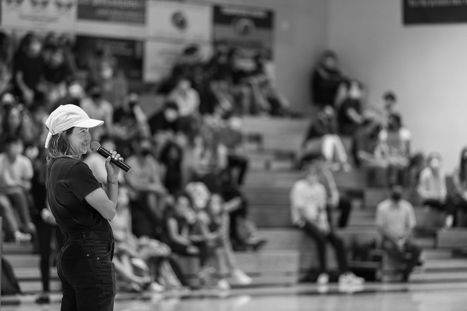 Black and white image of speaker addressing crowd in gymnasium setting.