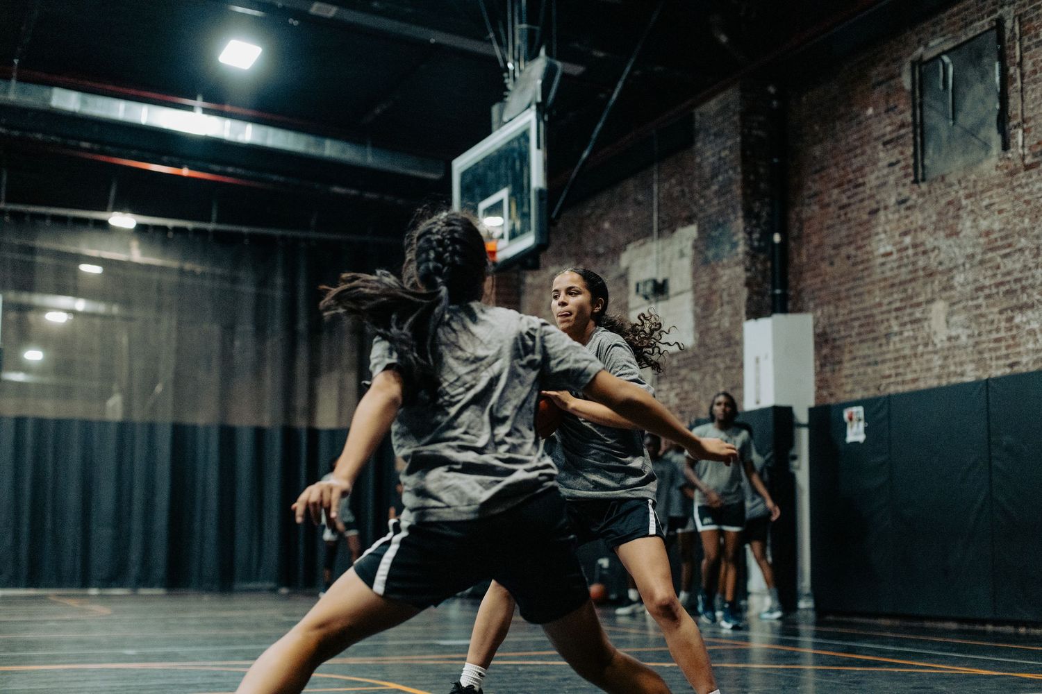 Basketball players practicing defensive moves in a dimly lit indoor court.