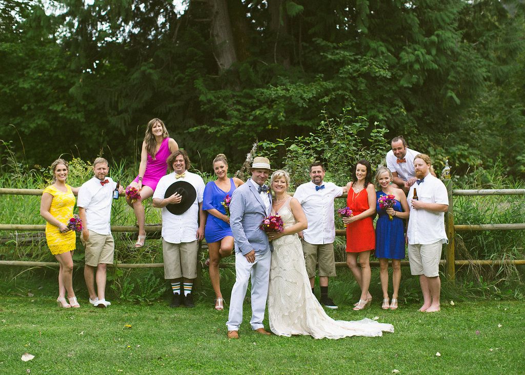 Wedding party members in coordinated outfits pose casually on a grassy lawn with trees in the background.