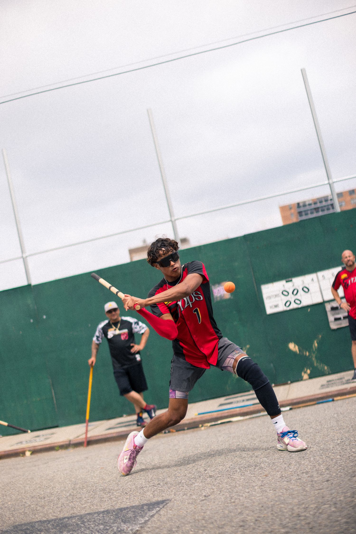 Baseball player in red jersey swings a bat during practice against green wall background.