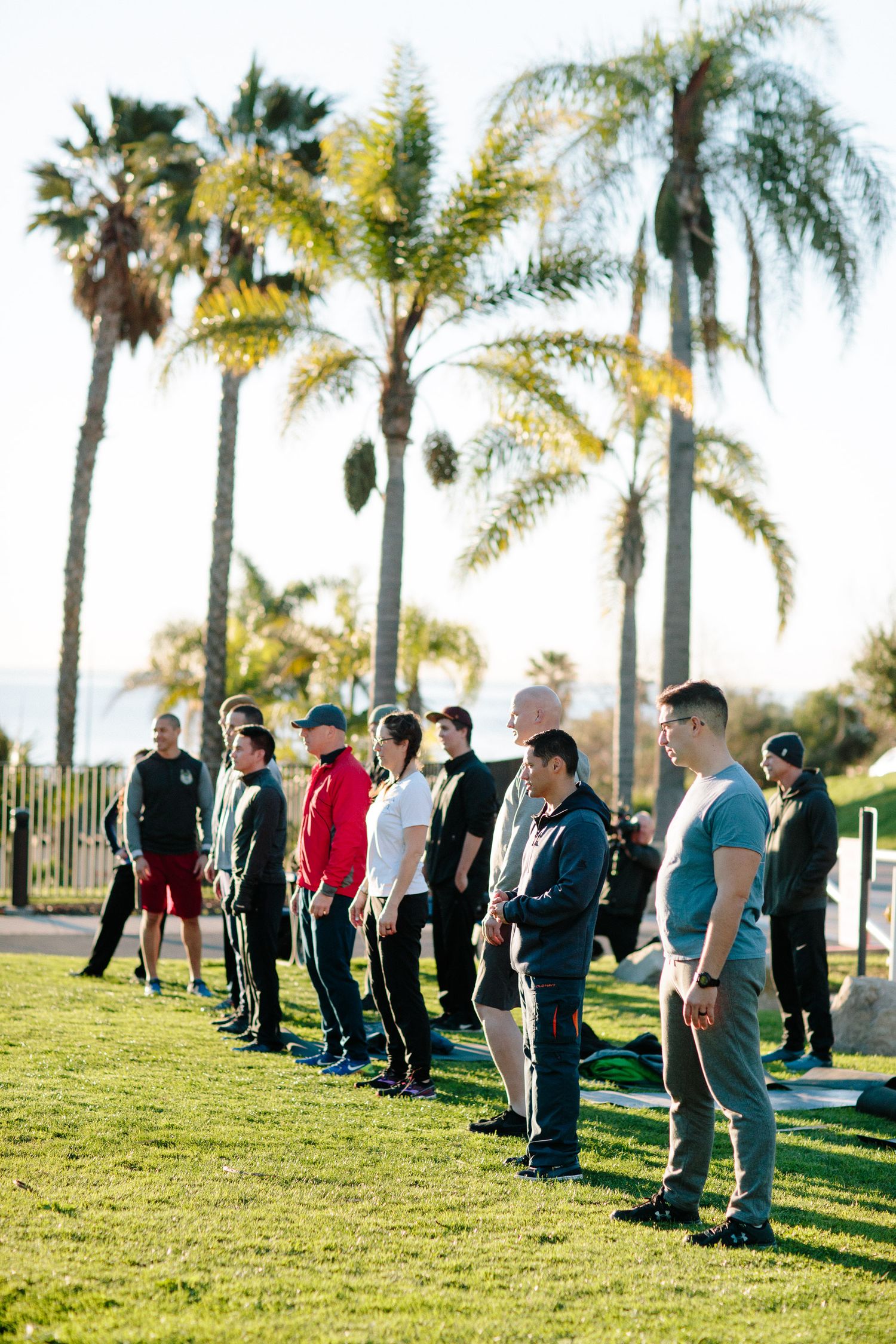 Group stands in formation on grass with palm trees lining the background.