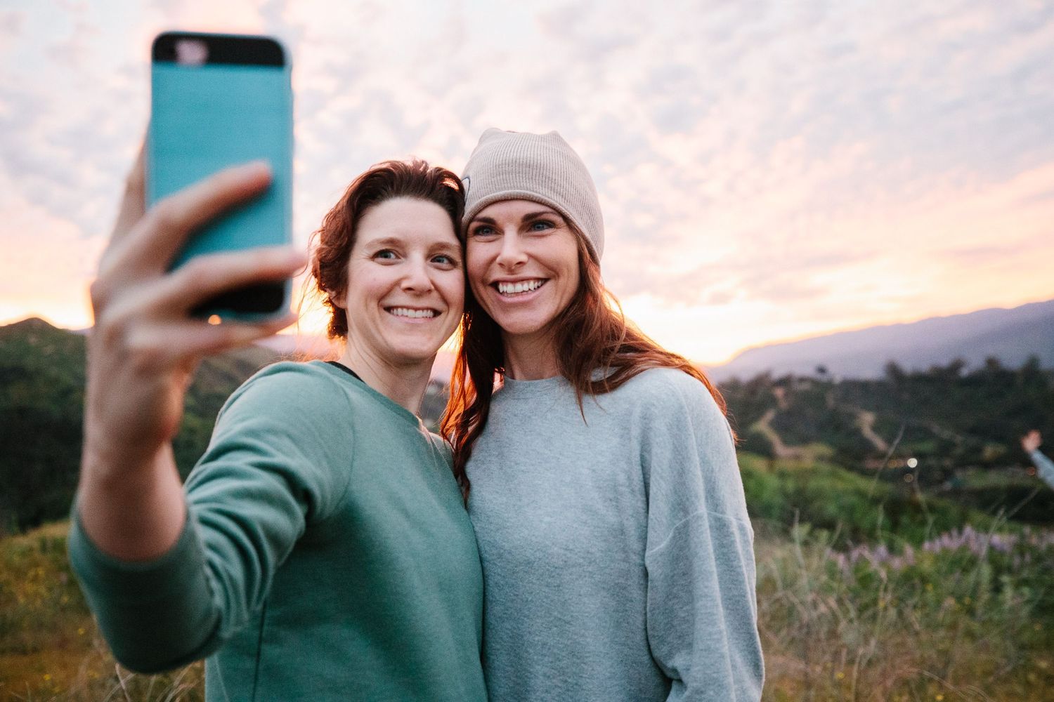 Two people taking a selfie together against mountain landscape at sunset.