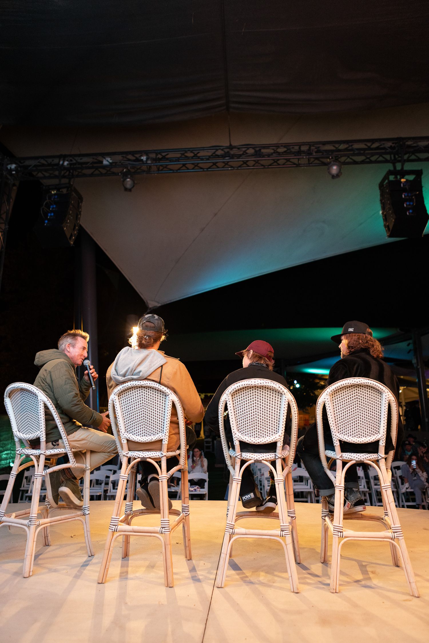A group sits on white bistro chairs at a bar or event space illuminated by blue-green stage lighting.