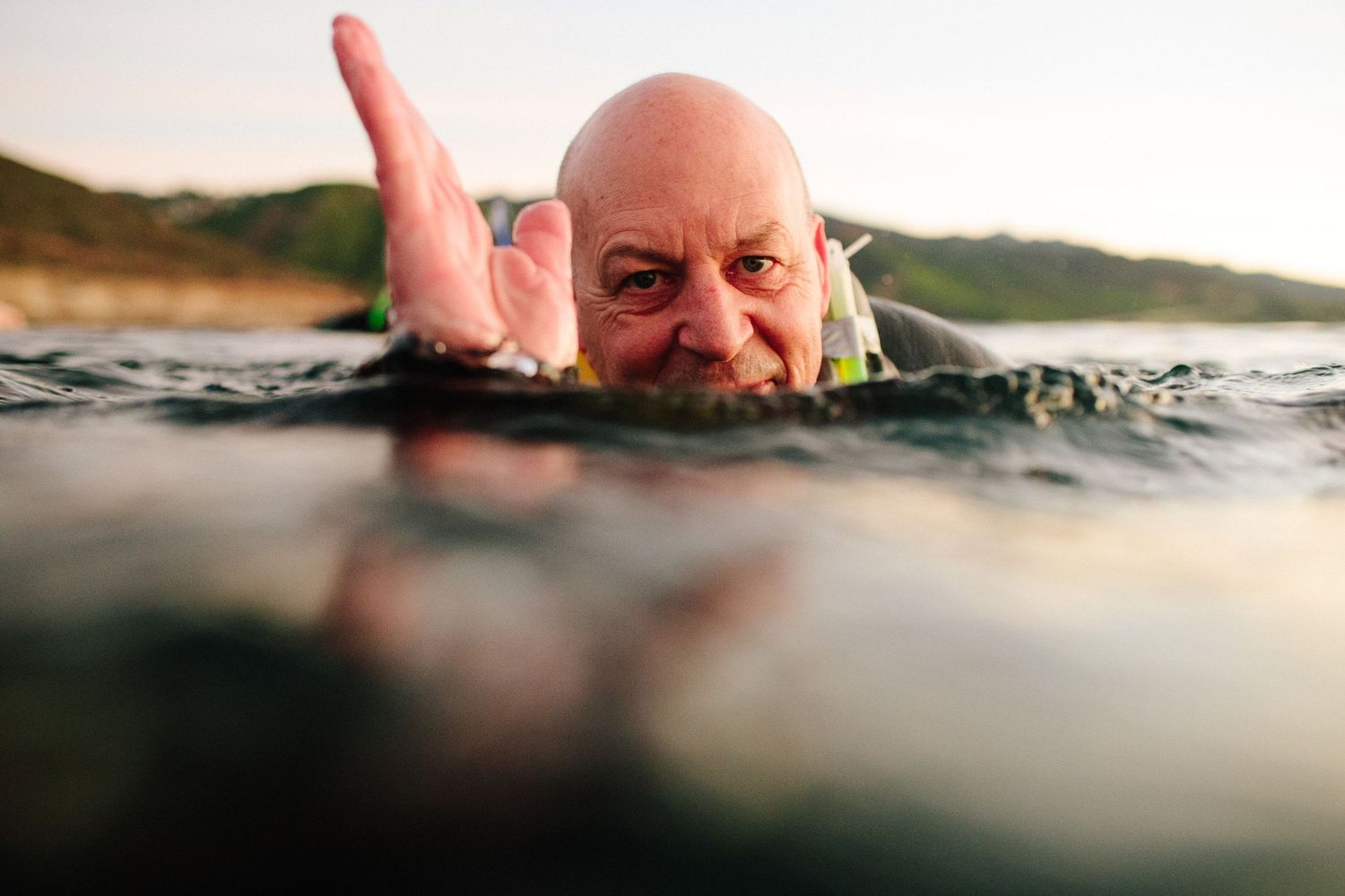 Close-up of someone emerging from water with hand raised during an outdoor swim.