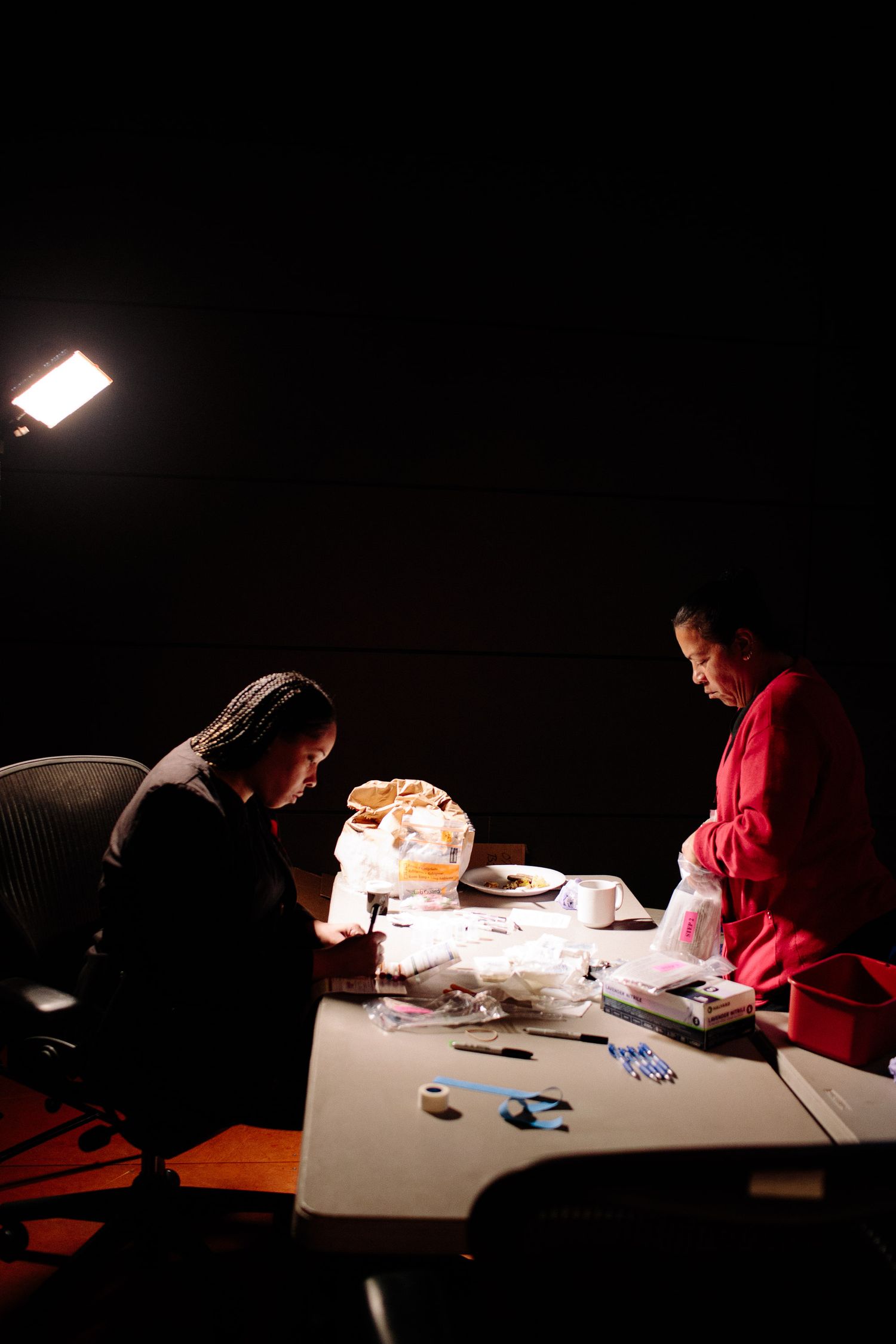 People work at a dimly lit table with documents and materials spread out.