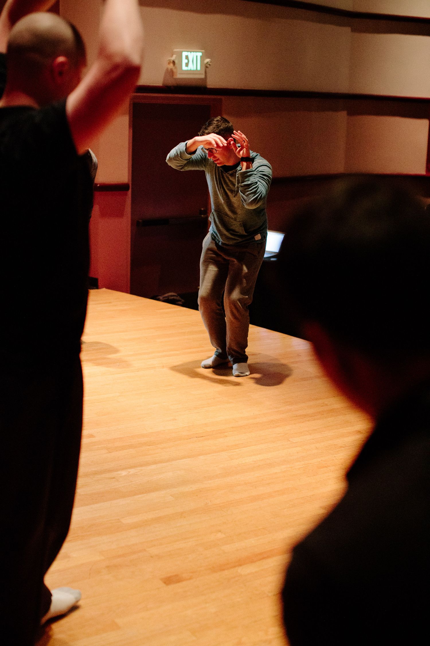 A performer on stage makes dramatic movements in a dimly lit theater space.