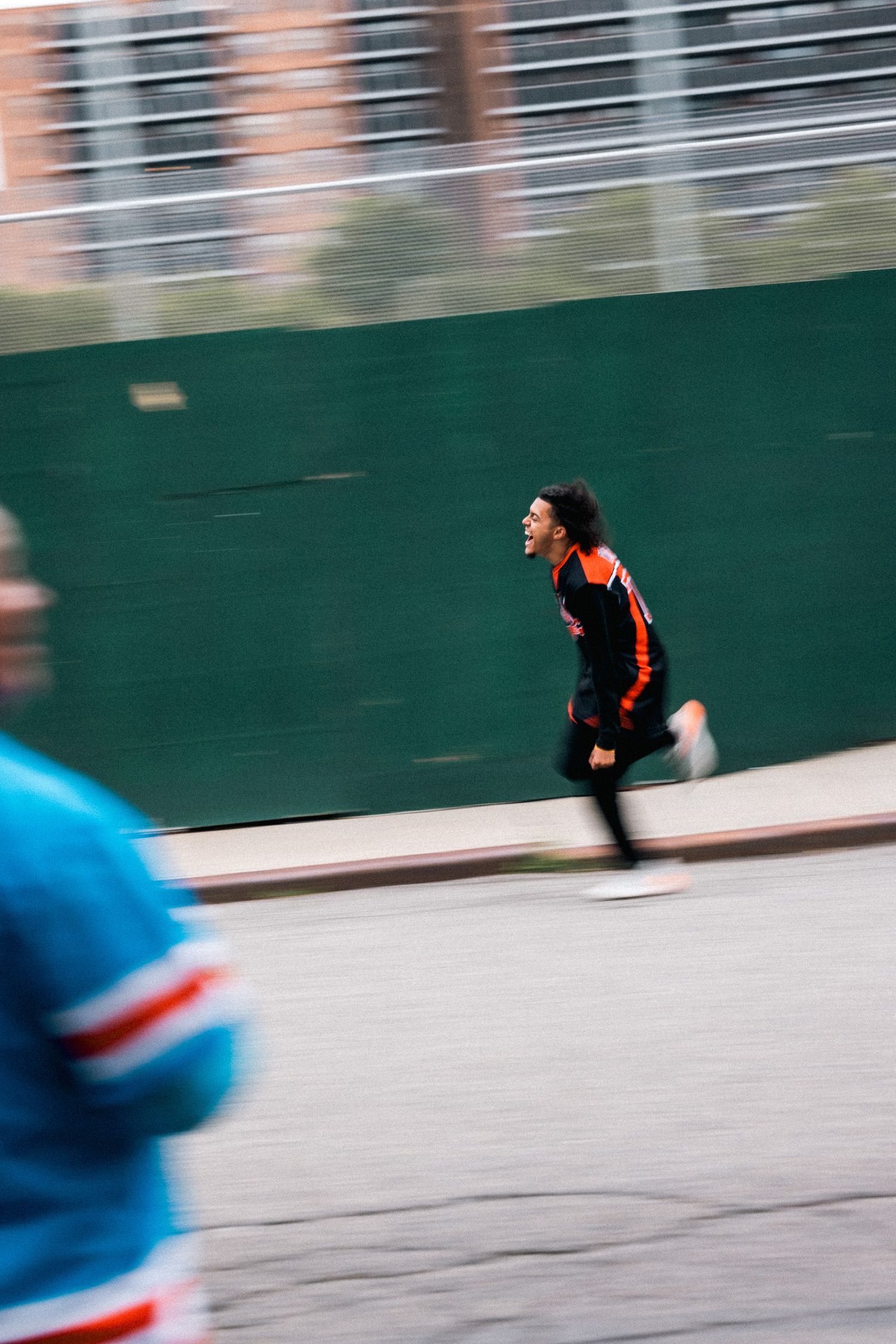 A person in black running past a green wall with motion blur effect.