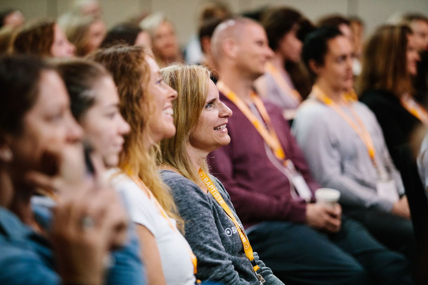 Engaged audience members watching and smiling during indoor presentation or performance.