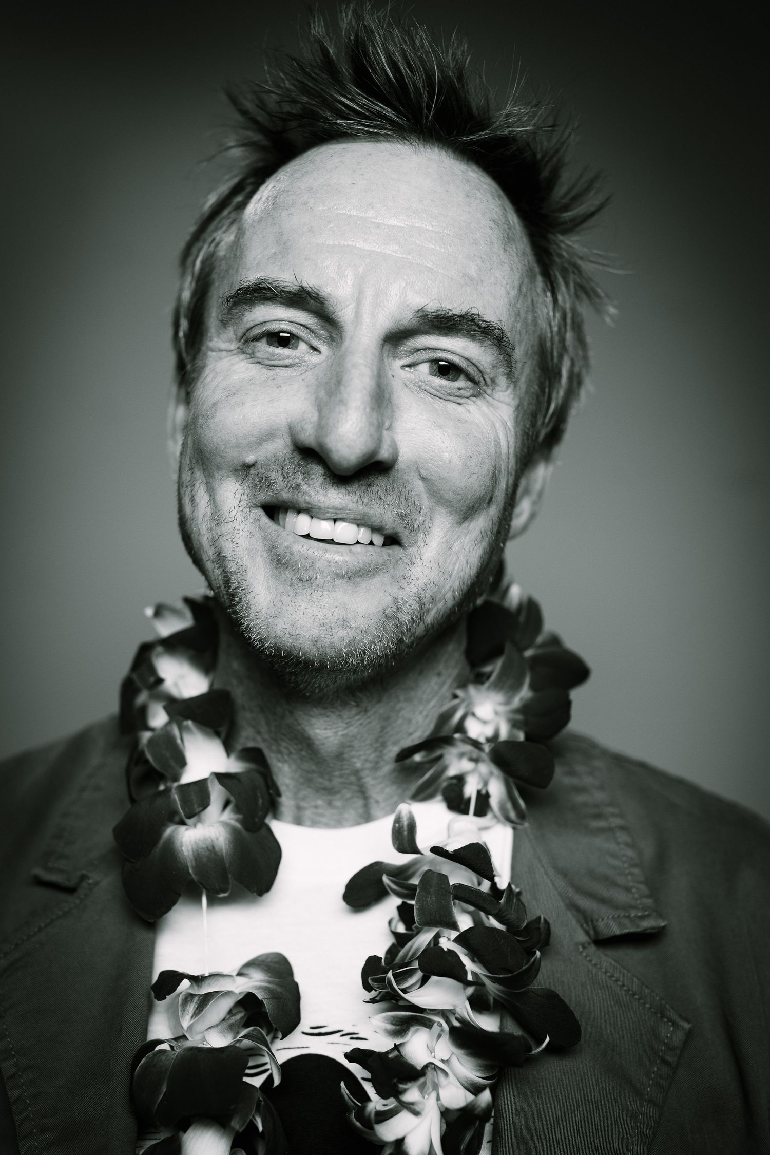 Black and white portrait showing a person with spiky hair wearing a floral lei and smiling warmly.