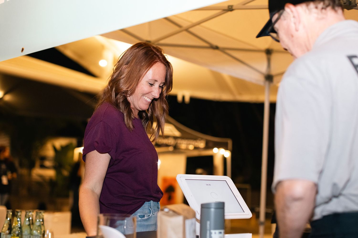 People interacting at an outdoor evening event under white canopy tents.