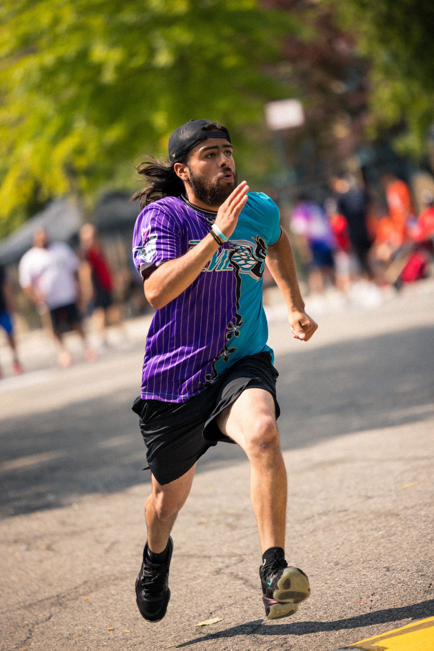 Runner in purple striped jersey and black shorts sprinting on outdoor pavement during competition.