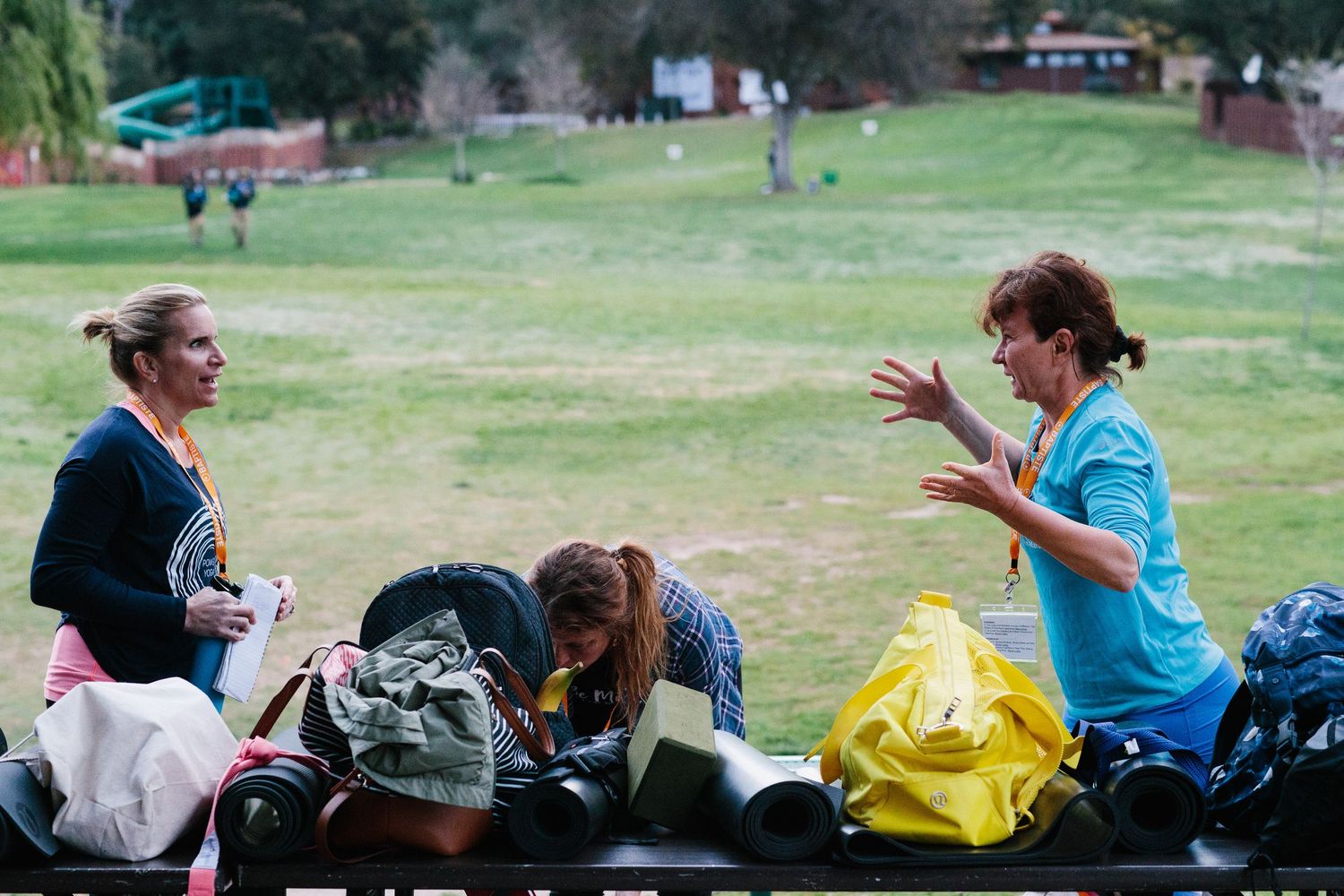 Spectators sit on a grassy hillside watching an event while others chat and socialize in the background.