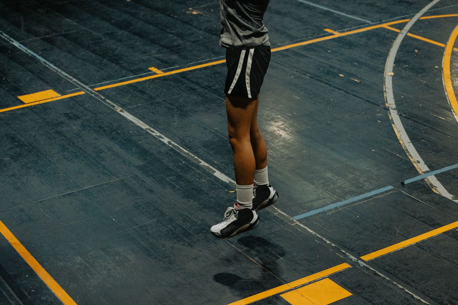 Legs of players standing on a basketball court marked with yellow lines and dark flooring.