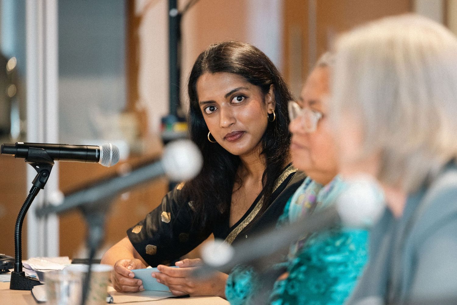 Two people sit at a table with microphones in what appears to be a radio studio or podcast recording setting.