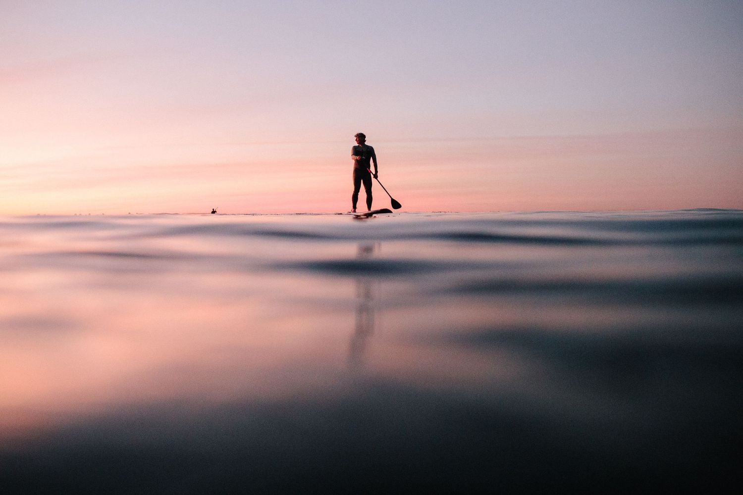 A peaceful ocean landscape at sunset with silhouetted figures on the horizon.