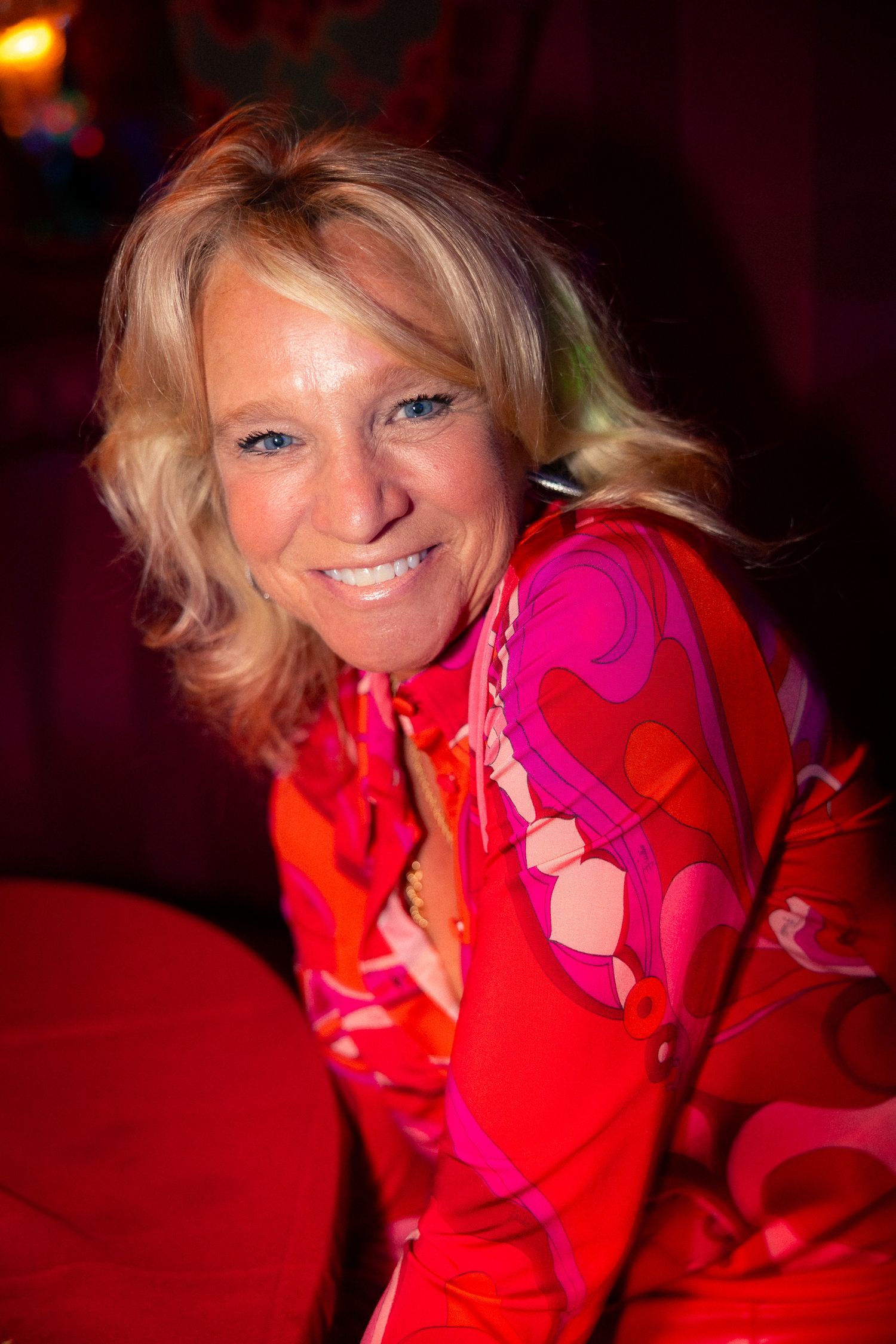 Woman in bright red attire poses playfully at an evening event.