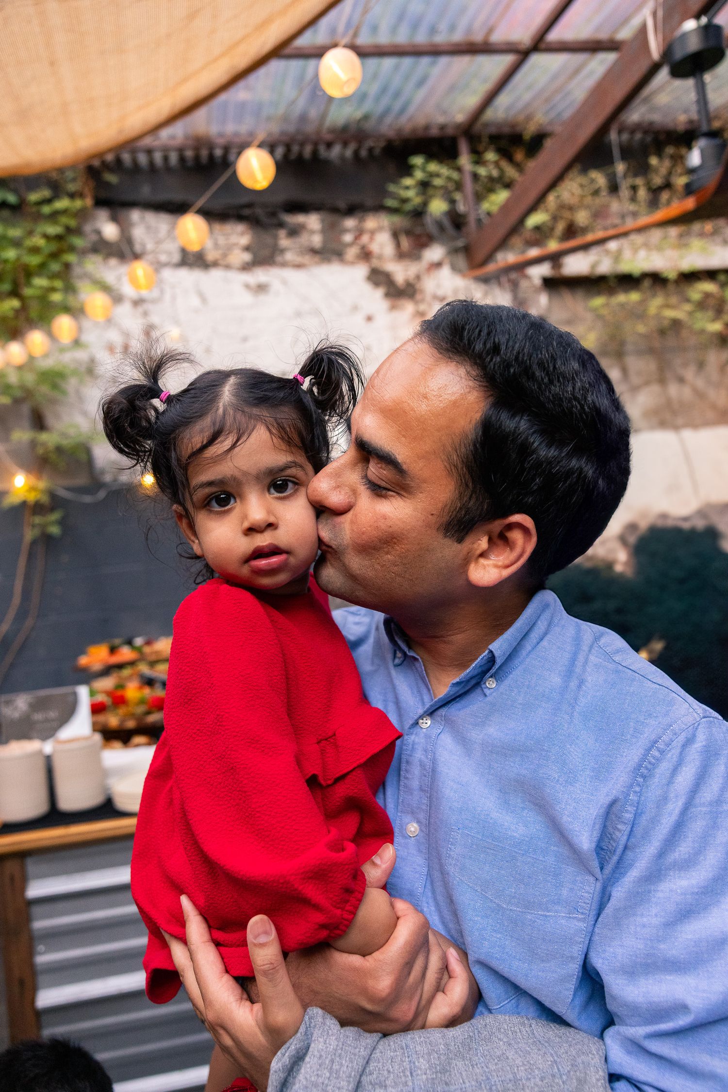 Parent and child sharing tender moment in red dress at outdoor gathering.
