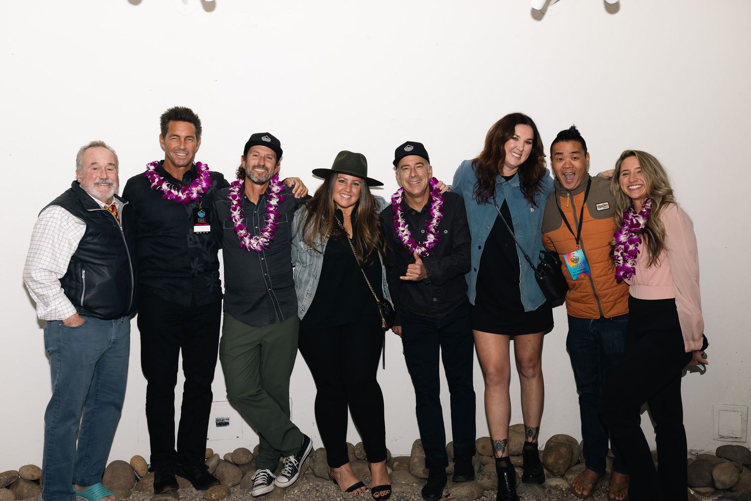Group photo of people standing against a white wall wearing casual attire and colorful leis.