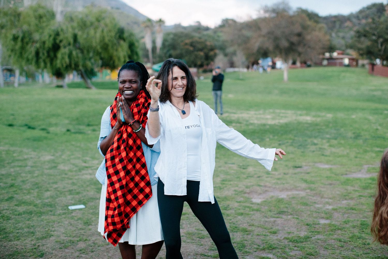 Two friends pose together on grassy field, one wearing red plaid and one in white shirt and black pants.