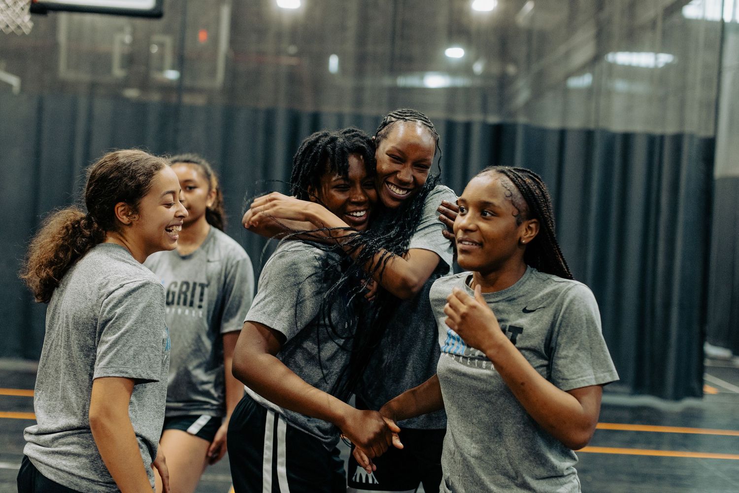 A group of athletes in gray t-shirts share a joyful moment together during practice in an indoor sports facility.