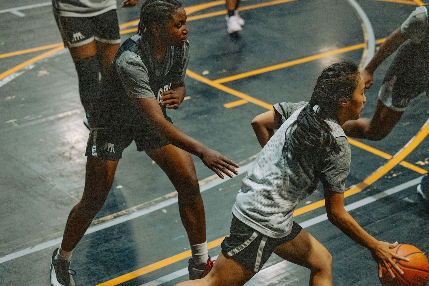 Basketball players compete intensely on indoor court during competitive game with focus on defensive action.