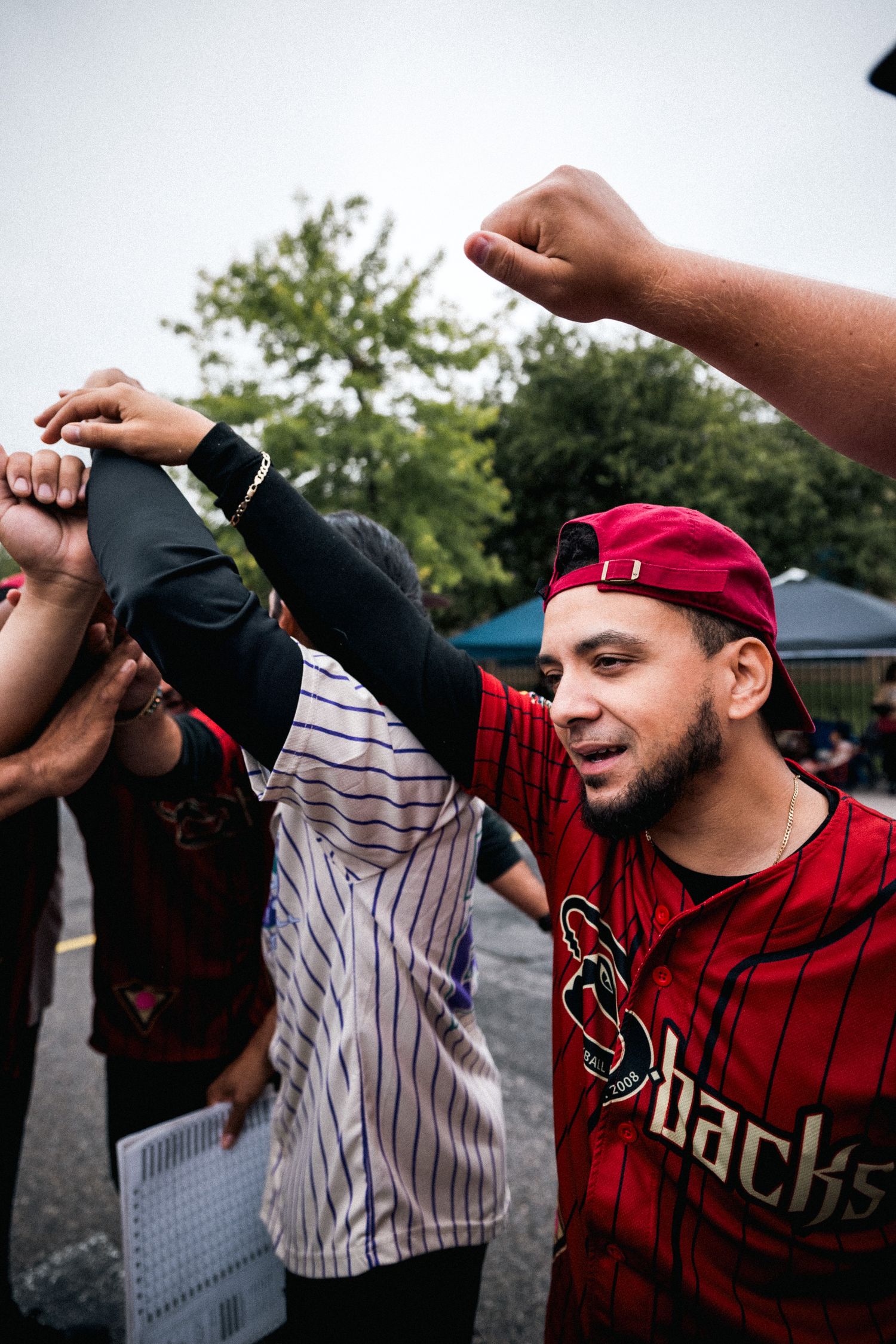 Baseball fans in team jerseys celebrate excitedly together at an outdoor gathering.