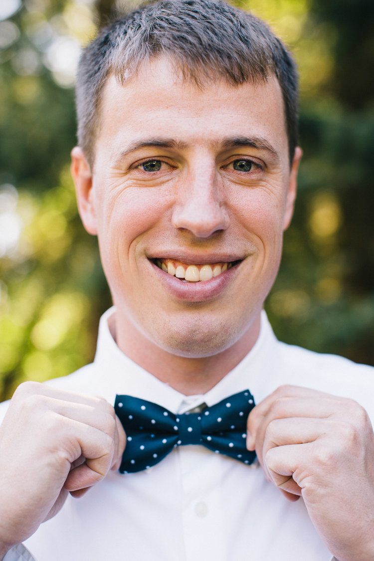 Person wearing a white dress shirt and polka dot bow tie smiling at the camera.
