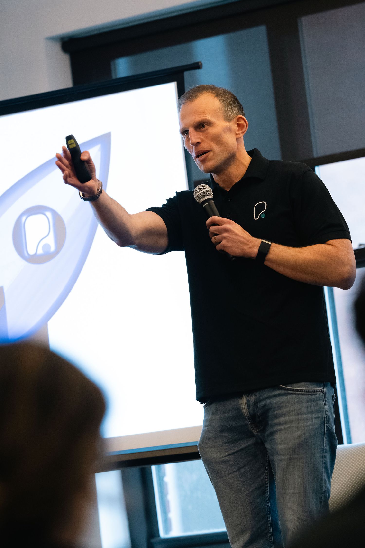 Speaker on stage gestures animatedly while presenting to an audience in a professional conference setting.