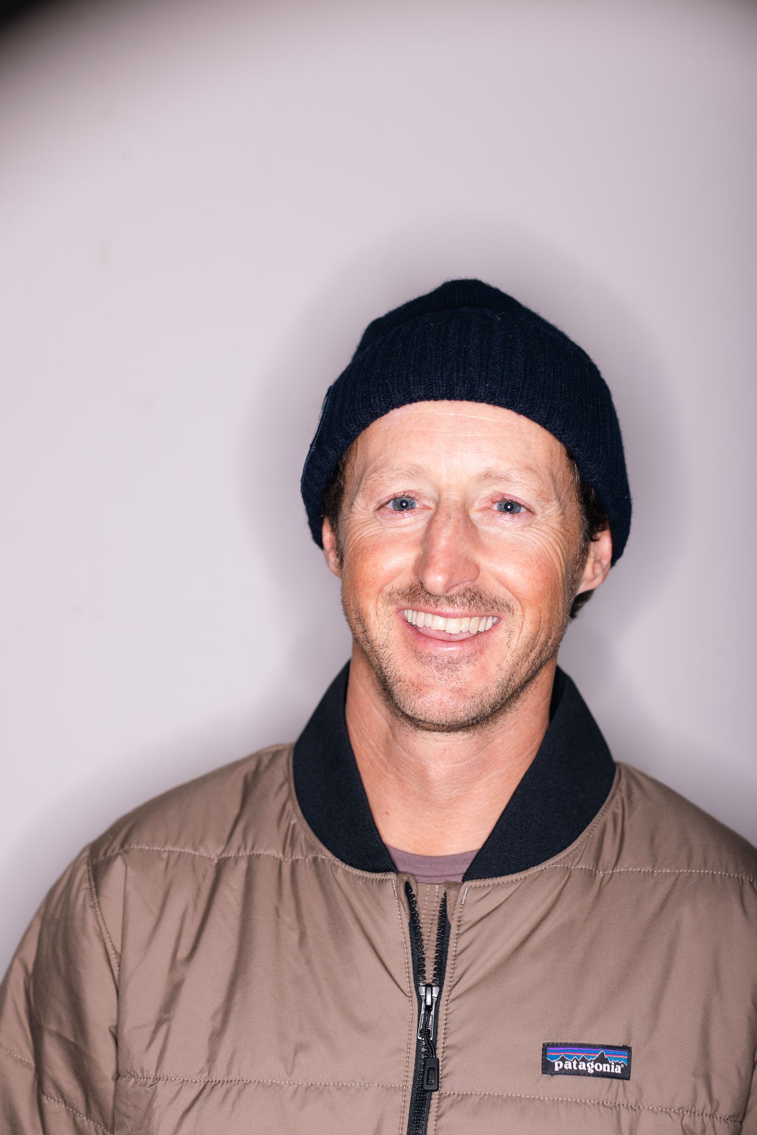 Studio portrait wearing a black beanie and tan Patagonia jacket against light background.