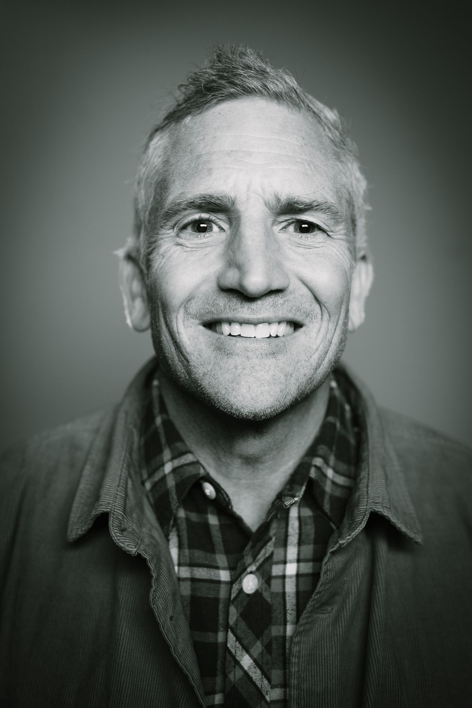 Black and white headshot of a person in a plaid shirt and jacket smiling at the camera.