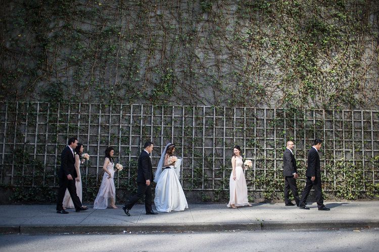 Wedding party walking and posing along a stone wall in formal attire.