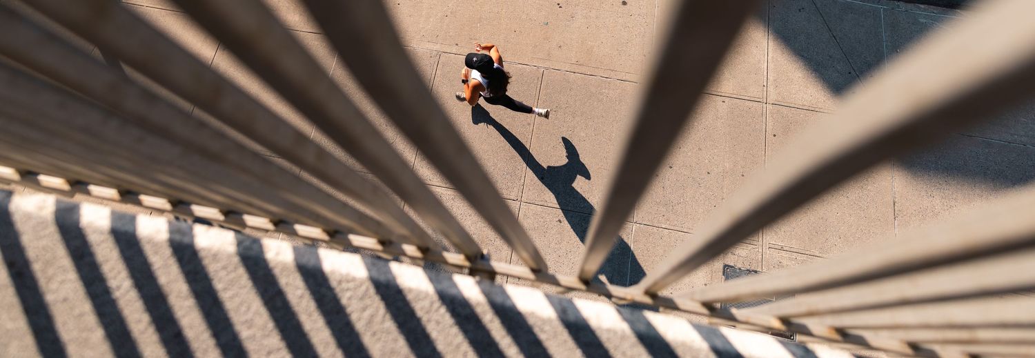 A person jumps in the air while casting dramatic shadows from vertical blinds on a concrete wall.