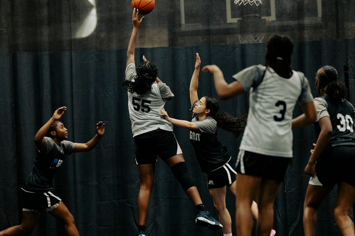 High school basketball players reach for the ball during an intense indoor game.